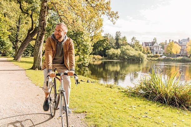 Man cyklar lugnt på en parkstig intill en damm i höstsol